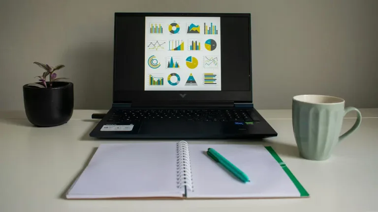 Laptop showing charts on screen with notebook and mug on a desk